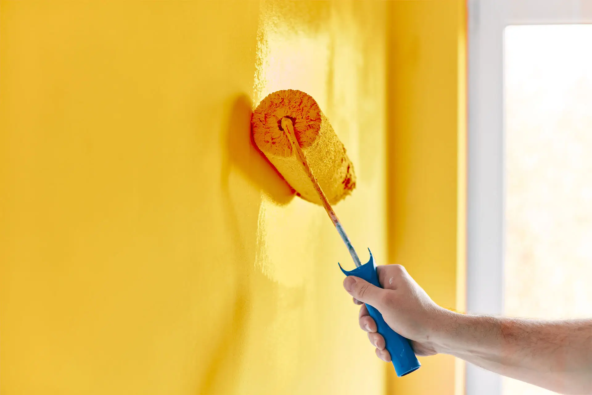 A person painting a yellow wall with a paintbrush, focused on applying an even coat of paint.