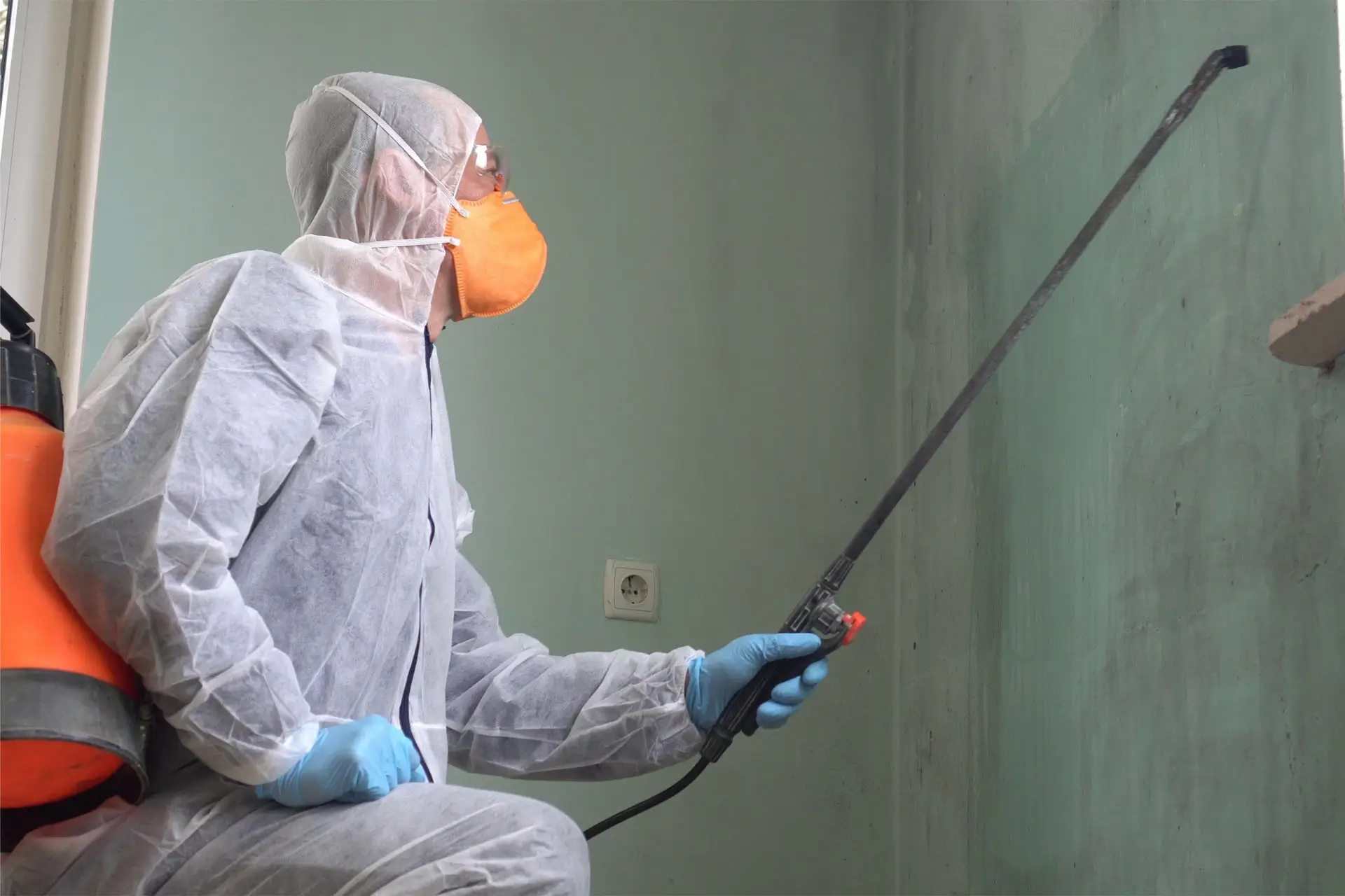 A man in a white suit applies spray paint to a wall, focused on his task.