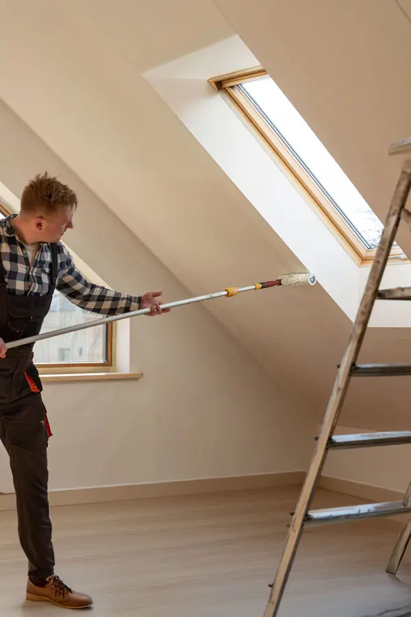 A man using a ladder to paint a room, focused on applying paint to the wall with a brush.