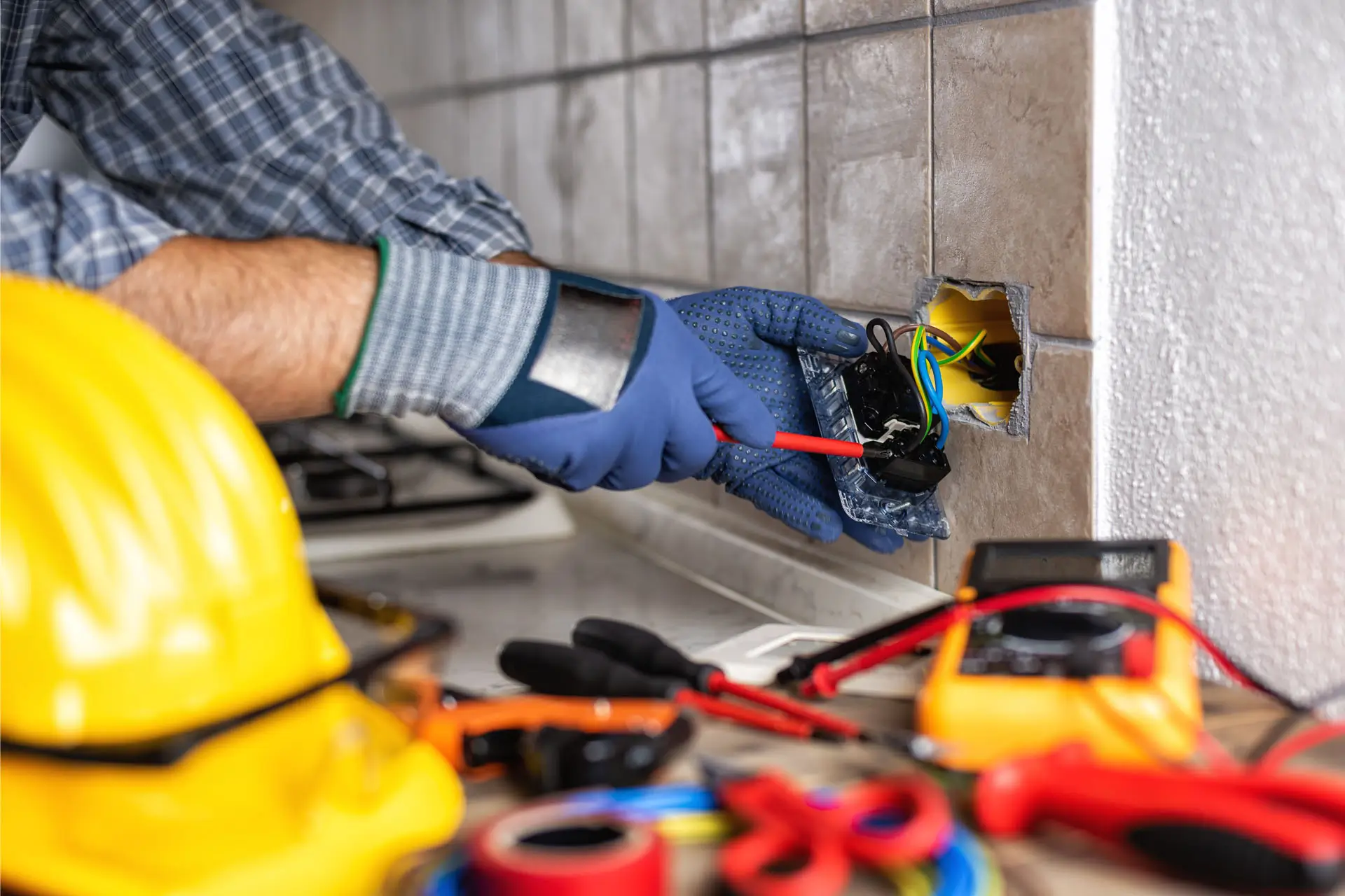 A man wearing a hard hat and gloves is actively working on a wall, demonstrating construction or repair tasks.